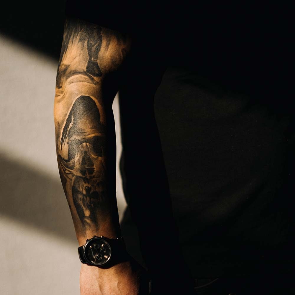 Primer plano del brazo tatuado de un peluquero, mostrando detalles artísticos que complementan su estilo profesional.